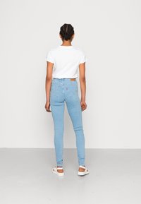 Ljusblå högmidjade jeans med bakfickor, kombinerat med en vanlig vit t-shirt med kort ärm och vita sandaler.