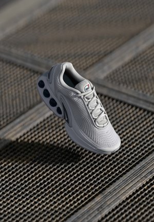 Light gray athletic shoe with a mesh upper, textured fabric, laces, and a rounded sole featuring visible air pockets.