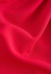 Tissu rouge vif et lisse avec de doux plis et une texture subtile créant des ombres et des reflets délicats.