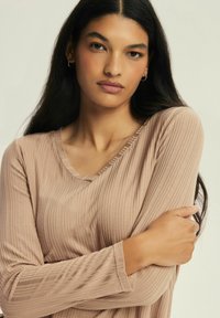 Long-sleeve ribbed top in soft beige fabric with a scoop neckline and slightly textured surface, featuring a relaxed fit and long, fitted sleeves.