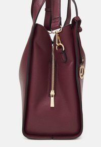 Sac en cuir bordeaux avec une finition texturée, équipé d'une fermeture éclair et de quincaillerie dorées, d'une poche latérale et d'un contour noir contrastant.