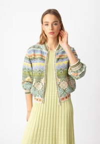 Daugiabriauni bomberis su gėlių raštais, su užtrauktuku ir gumuotomis rankovėmis. Nešiojamas virš plisuotos žalios suknelės.