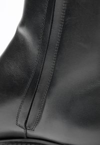 Černá kožená kotníková bota s hladkým povrchem, viditelným švem podél švů a elegantním designem bez kovových doplňků nebo vzorů.