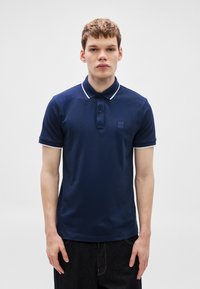 Tricou polo albastru marin din țesătură texturată, cu guler cu accente albe, fenta cu trei nasturi și o mică emblemă pe piept.
