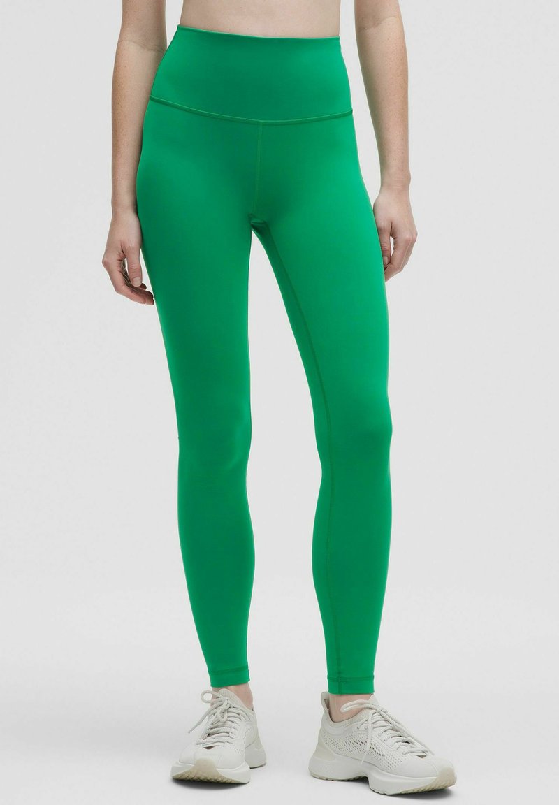Gröna högmidjade leggings gjorda av stretchigt tyg, med en slät yta och passform, parat med lätta sneakers.