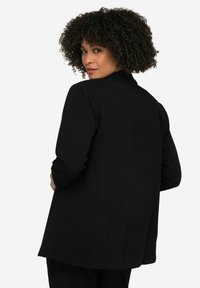 Blazer noir à manches longues, au design structuré et à la coupe droite. Tissu lisse avec une texture subtile et des lignes épurées au dos.