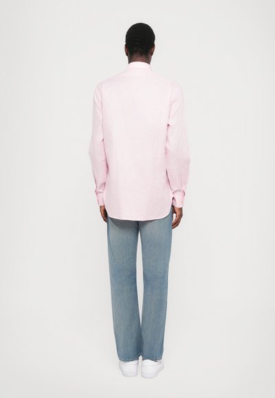 Απαλή ροζ μακρυμάνικη πουκάμισα με διακριτό καρό σχέδιο, συνδυασμένο με ανοιχτό μπλε φαρδύ τζιν παντελόνι και λευκά αθλητικά παπούτσια, σε θέα από πίσω.