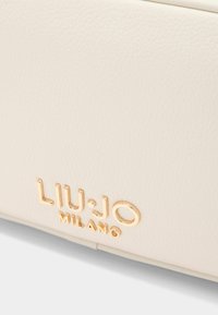 Valkoinen nahkalaukku, jossa on kohokuvioitu "LIU·JO MILANO" -logo kullassa, sileä pinta ja hienovarainen tekstuuri.