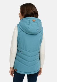 Light blue puffer vest with a hood, featuring chevron stitching details and a brown leather logo at the back, paired with a white top.