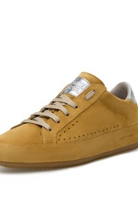Sneaker in suede giallo senape con una texture liscia, lacci beige, un patch logo in metallo argentato e dettagli perforati sui lati.