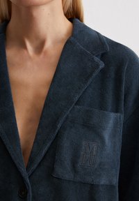 Navy textured blazer with a lapel collar, single button closure, and a chest pocket featuring an embroidered logo detail.
