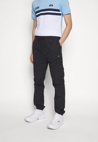 Mustat cargo-housut joustavalla vyötäröllä, sivutaskut, yhdistettynä vaaleansiniseen ja tummansiniseen polo-paitaan, sekä valkoisiin lenkkareihin.