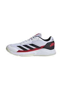 Chaussure de sport blanche avec des accents noirs et rouges. Présente une tige en mesh, une semelle texturée et trois rayures noires sur le côté.