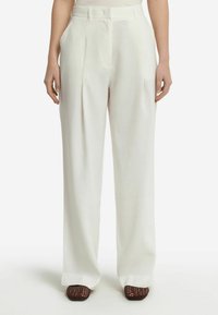 Pantaloni a vita alta plissettati in morbido tessuto bianco, con una silhouette a gamba dritta e tasche laterali, abbinati a scarpe intrecciate marroni.