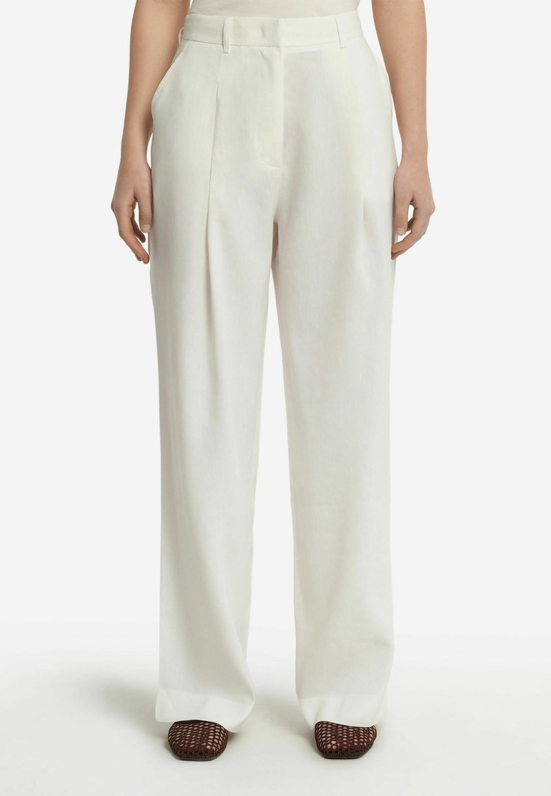 Pantaloni a vita alta plissettati in morbido tessuto bianco, con una silhouette a gamba dritta e tasche laterali, abbinati a scarpe intrecciate marroni.