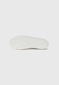 Semelle de sneaker en caoutchouc blanc avec un motif de grip texturé et un logo en relief. Surface lisse aux bords arrondis. Design minimaliste.