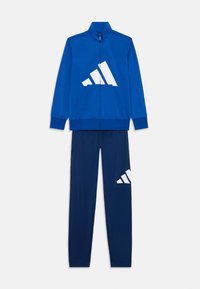 Survêtement de sport bleu comprenant une veste zippée avec un grand logo blanc et un pantalon fuselé assorti avec un logo blanc sur la jambe.
