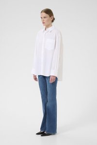 Oversized white button-up shirt with a chest pocket, paired with flared blue denim jeans and black pointed-toe shoes. Smooth texture.