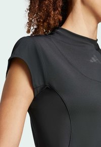 Svart atletisk topp med en figurnära design, korta ärmar, slät yta och plattlåst sömmar; har en diskret logotyp på övre bröstet.