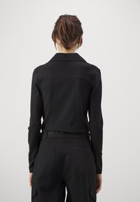 Fekete, rövidített dzseki hosszú ujjal és gallérral, sima anyagból készült. Minimalista dizájn jellemzi, nincs látható fémszerelvény vagy minta.