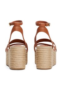 Brown leather wedge sandals with a woven jute platform, featuring multiple straps and a buckle closure at the ankle.