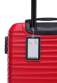 Red hard-shell luggage with vertical ridges, retractable black handle, and a clear tag holder displaying name and contact fields.