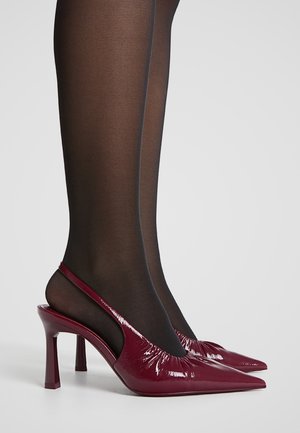Escarpins slingback en cuir verni bordeaux avec un bout pointu, finition brillante et un collant noir texturé comportant une couture verticale.