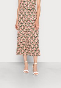 Woman wearing a midi skirt with a pink, green, and white floral pattern paired with white braided high-heeled sandals.