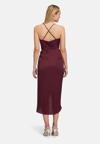 Fioletowa sukienka o kroju ołówkowym, sięgająca do połowy łydki, z cienkimi krzyżującymi się ramiączkami oraz rozcięciem z tyłu dla ułatwienia ruchów. Gładki satynowy materiał.