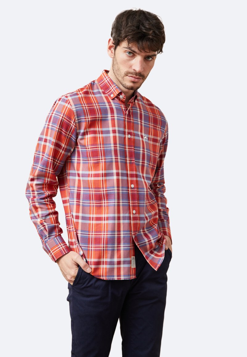 Camisa de cuadros roja y azul en tejido de algodón con cuello abotonado y logo en el pecho, combinada con pantalones oscuros.