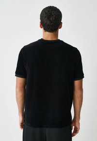 Schwarzes, geripptes Kurzarm-T-Shirt mit rundem Ausschnitt und strukturiertem Stoff. Hat ein schlichtes Design und dezente Saumdetails.