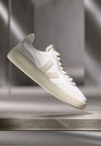 Sneakers bianchi con una tomaia liscia arricchita da dettagli in rete, suola in gomma beige e un grande logo V beige sul lato.