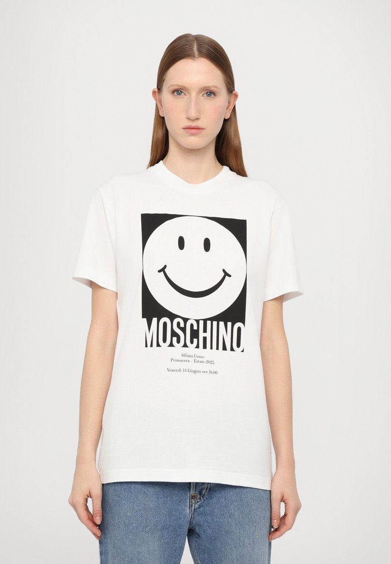 Bílá bavlněná tričko s velkým černým smajlíkem a textem "MOSCHINO", s volným střihem a krátkými rukávy.