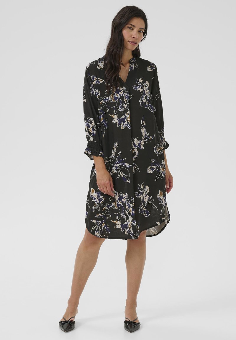 Rochie neagră cu un model floral în nuanțe de violet și crem. Dispune de un decolteu în V, mâneci lungi cu manșete strânse și o margine de lungime a genunchiului.