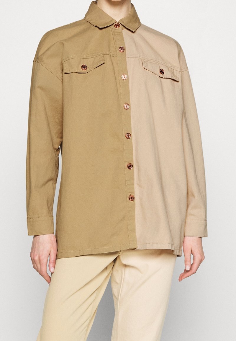 Chemise à manches longues boutonnée avec deux poches poitrine, moitié marron clair et moitié beige, portée avec un pantalon beige clair.