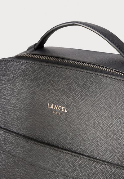 Черен текстуриран кожен чанта с горна дръжка, видим цип и златно лого "Lancel Paris" на предната повърхност.