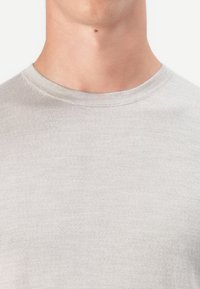 Nacken und oberer Brustbereich einer Person, die einen hellgrauen Rundhalsausschnitt-Pullover trägt, mit einem kleinen Muttermal in der Mitte unter dem Kinn.