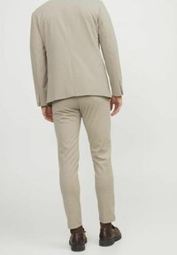 Béžová slim fit sako a kalhoty z hladkého materiálu, se strukturovanou siluetou, jednoduchým zadním dílem a tmavě hnědými botami.