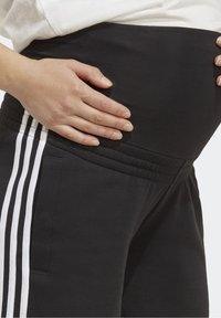 Svarta gravidbyxor med bred elastisk midjeband och tre vita ränder längs sidan; tyget verkar mjukt och stretchigt.