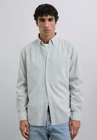 Camisa verde claro de botones con cuello, mangas largas y corte relajado, combinada con pantalones de mezclilla azul claro. Textura suave.