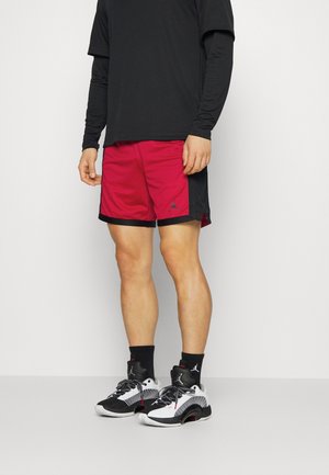 Rode en zwarte sportshorts met zakken, een zwart T-shirt en zwart-witte sneakers. De shorts hebben een logo en een textuurstof.