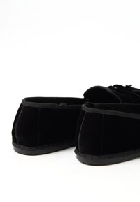 Pantuflas de terciopelo negro con un perfil bajo, que cuentan con una textura suave, ribete negro y suelas de goma para un agarre antideslizante.