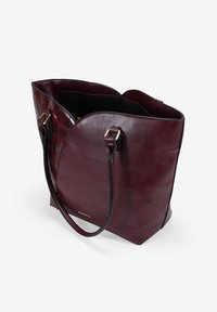 Bolso tote de cuero burdeos con una textura suave y una parte superior curvada distintiva. Presenta herrajes en tono dorado y un interior negro. Base plana.