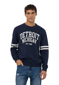 Granatowy sweter z napisem "DETROIT MICHIGAN EST. 1982" w kolorze białym, z białymi paskami na rękawach. Wykonany z miękkiego materiału bawełnianego, o luźnym kroju.