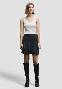 Biely tielkový top, čierna mini sukňa s volánikovým detailom a diagonálnymi pruhmi, doplnené čiernymi čižmami po kolená. Jednoduchý dizajn, priliehavý strih.