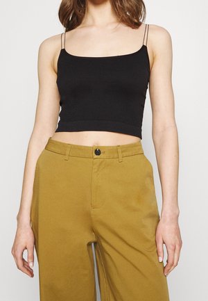 Czarny prążkowany krótki top na cienkich ramiączkach, zestawiony z wysokim stanem musztardowych spodni z zapięciem na guziki i bocznymi kieszeniami.