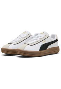 Baskets blanches avec des accents en daim noir, bout beige et marquage doré. La semelle est brune avec un motif de grip texturé.
