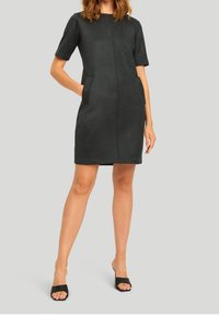 Schwarzes Kurzarmkleid aus weichem, wildlederähnlichem Material, mit einer Mittelnaht und seitlichen Taschen. Schlichte, figurbetonte Passform mit minimalistischem Design.