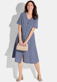 Navy- und weißkariertes Midi-Kleid mit kurzen Ärmeln, Knopfverschluss vorne und Seitenschlitzen. Model hält eine beige Clutch und trägt Riemchensandalen.