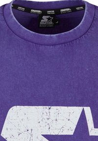 T-shirt court violet à manches courtes avec un col rond, présentant un design graphique blanc usé d'une étoile sur le devant. Texture douce.
